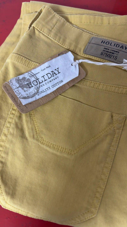 Etichetta Holiday Jeans Company su pantalone ocra piegato su fondo rosso