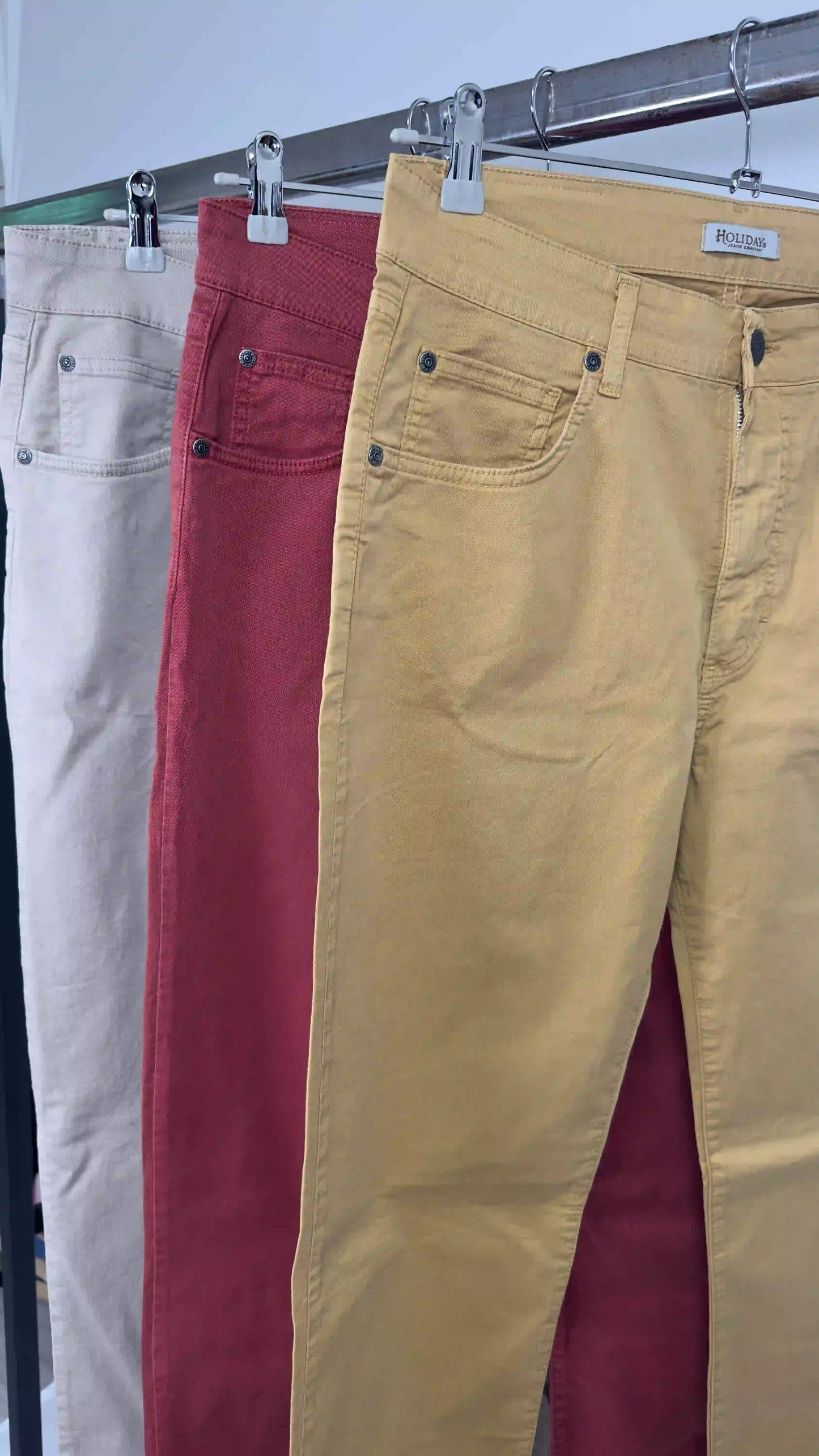 Tre pantaloni Holiday ocra rosso e beige appesi insieme su barra metallica